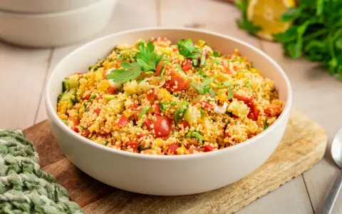 Frischer Couscous Salat mit Tomaten, Gurken und Paprika, garniert mit Petersilie. Ein leichter und gesunder Genuss.