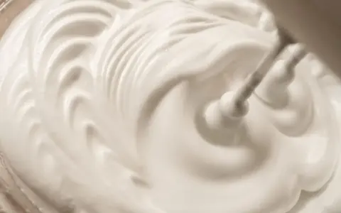 Schlagende Sahne wird mit einem Handmixer zu steifen Spitzen aufgeschlagen, bereit für köstliche Desserts.
