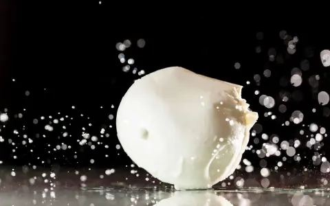 Ein frischer Fior di Latte, der auf einer spiegelnden Oberfläche liegt, umgeben von Wassertropfen und Bokeh-Lichtern.
