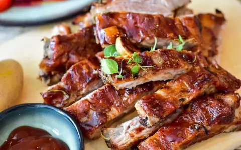 Saftige Spareribs mit glänzender Marinade, garniert mit frischen Kräutern. Dazu eine Schale BBQ-Sauce und eine Kartoffel.