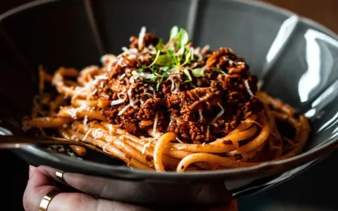 Eine Schüssel mit herzhaftem Pasta al Ragu, garniert mit frischen Kräutern und geriebenem Käse.