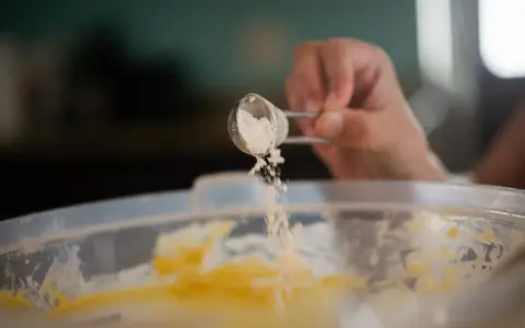 Eine Hand streut Natron aus einem Löffel in eine Schüssel mit Teig. Perfekt für das Backen!