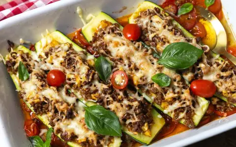 Gefüllte Zucchini mit Hackfleisch, überbacken mit Käse und garniert mit Tomaten und Basilikum. Ein köstliches Gericht!