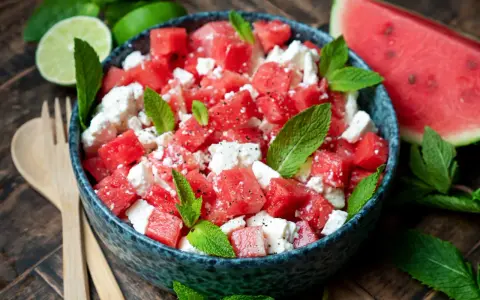 Erfrischender Wassermelonensalat mit Feta und Minze, perfekt für ein leichtes sommersalat rezept. Dazu passen Limettenspalten und Holzbesteck.
