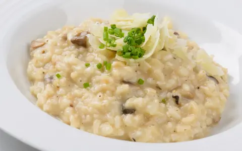 Cremiger Pilz-Risotto-Reis, garniert mit Parmesan und Schnittlauch, serviert in einer weißen Schüssel.