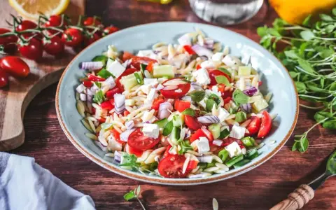 Frischer Kritharaki Salat mit Tomaten, Gurken, Feta und roten Zwiebeln, garniert mit Kräutern. Ein leichter Genuss!