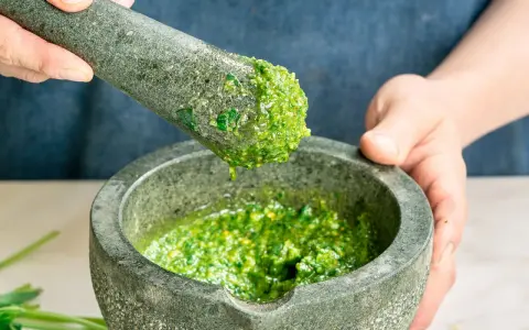 Frische Kräuter werden im Mörser zu einem leuchtend grünen pesto genovese zermahlen.