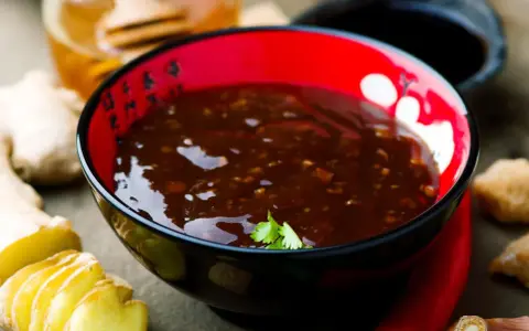 Schwarze Schüssel mit glänzender Teriyaki-Sauce, umgeben von Ingwer, Chili und Honig. Perfekt für dein Teriyaki Sauce Rezept!