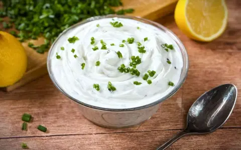Cremige **sour cream** garniert mit Schnittlauch, daneben Zitronenspalten und ein Löffel.