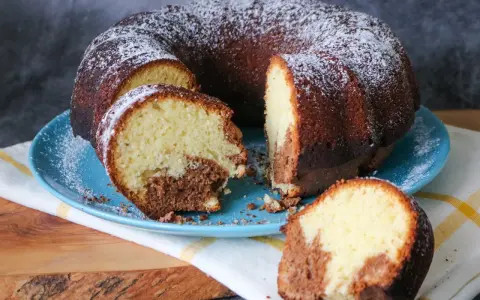 Saftiger weltbester Marmorkuchen, mit Puderzucker bestäubt, auf blauem Teller, ein Stück abgetrennt.
