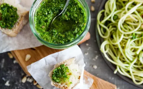 Frisches Basilikumpesto rezept in einem Glas, daneben Brot mit Pesto und eine Portion Spaghetti. Perfekt für ein schnelles Mittagessen.