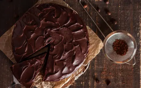 Ein saftiger Nutella Kuchen mit dunkler Schokoladenglasur, ein Stück wurde bereits entnommen. Daneben ein Sieb mit Kakaopulver.