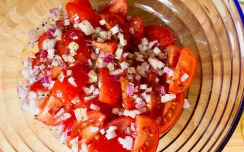 Frischer Tomatensalat mit roten Zwiebeln und Kräutern, bereit für Feta.