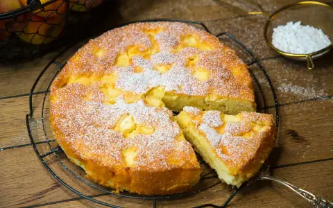 Ein saftiger, versunkener Apfelkuchen nach Omas Rezept, bestäubt mit Puderzucker. Ein Stück wurde bereits herausgenommen.