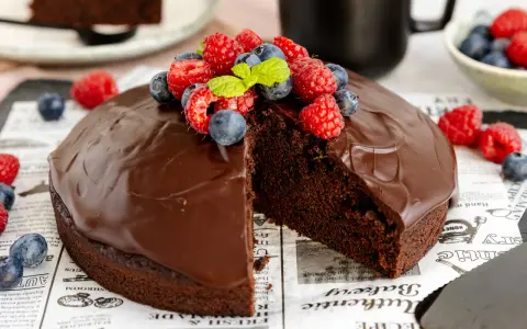 Ein saftiger veganer Schokokuchen mit glänzender Schokoladenglasur, garniert mit frischen Himbeeren und Blaubeeren.
