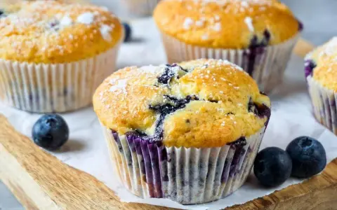 Frisch gebackene Blaubeer Muffins, bestäubt mit Puderzucker, liegen auf einem Holzbrett.