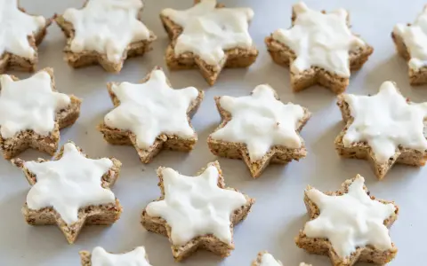 Klassisches zimtsterne rezept: Sterne aus Nüssen, mit weißer Glasur überzogen, bereit zum Genießen.