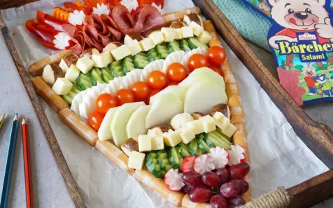 Bunter Fingerfood-Käse-Wurst-Teller in Pizzastückform, perfekt für die Einschulung. Mit Würstchen, Käse, Gurken, Tomaten, Radieschen, Trauben und Salami.