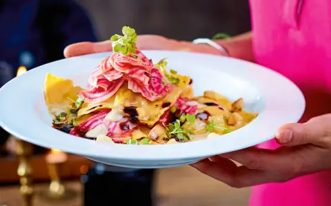Ein Teller mit Ravioli, garniert mit Streifen von roter Bete und Kräutern. Ein Gericht, das perfekt für "Das perfekte Dinner Rezepte" wäre.