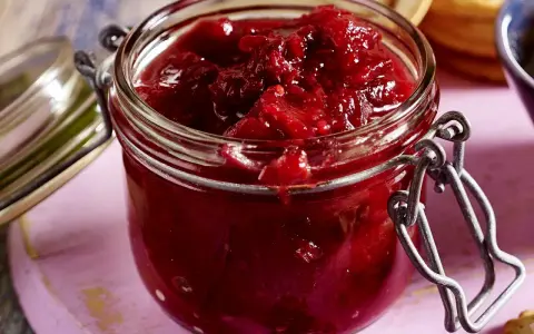 Ein Glas mit leuchtend rotem Zwetschgen-Chutney, bereit, zu Käse oder Gebäck serviert zu werden.