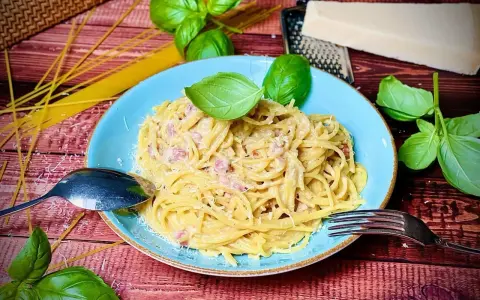 Herzhafte Spaghetti Carbonara mit Speck, garniert mit frischem Basilikum und Parmesan. Ein Klassiker, der immer schmeckt.