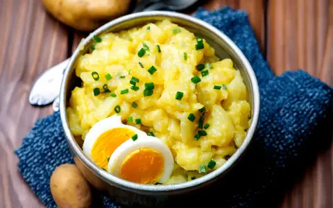 Schüssel mit warmem Kartoffelsalat, garniert mit Schnittlauch und Ei. Ein herzhaftes Gericht, das zum Genießen einlädt.