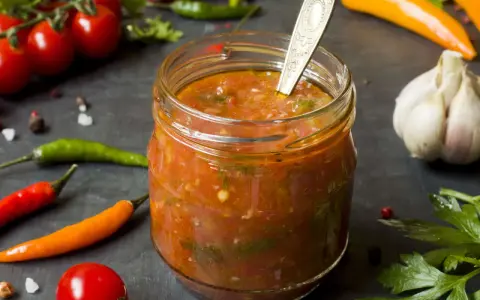 Ein Glas mit würzigem Zucchini-Ketchup, umgeben von frischen Tomaten, Chilis und Knoblauch.