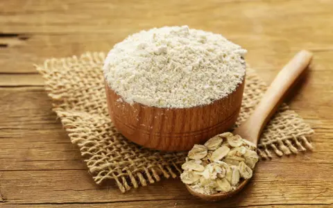 Holzschale mit feinem Hafermehl und Löffel voller Haferflocken. Perfekt zum Backen mit Hafermehl.