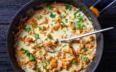 Pfifferlinge in cremiger Rahmsauce, garniert mit Petersilie, in einer Pfanne. Ein Löffel ragt aus der köstlichen Speise.