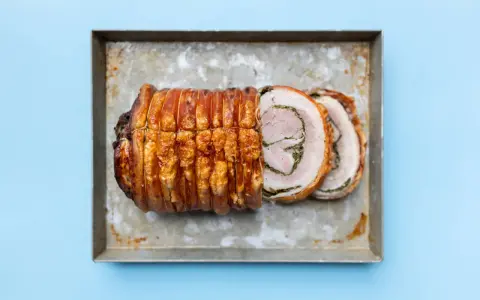 Ein knusprig gebratenes Stück Porchetta, ein italienisches Schweinebraten-Gericht, liegt auf einem Blech.