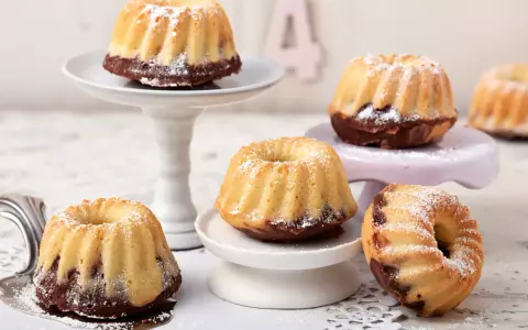 Mehrere kleine, mit Puderzucker bestäubte Mini Gugelhupf-Kuchen mit Schokoladenboden stehen auf verschiedenen Etageren.