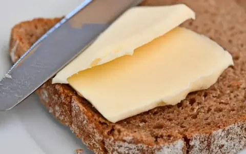 Ein Messer verteilt cremige Butter oder Margarine auf einer Scheibe dunklem Brot.