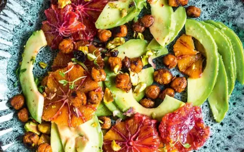 Ein bunter Avocado-Salat mit Blutorangen, Kichererbsen und Pistazien auf einem rustikalen Teller.