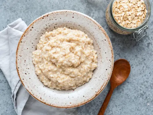 Cremiger Haferbrei im Teller, daneben ein Glas Haferflocken und ein Holzlöffel. Perfekt für ein einfaches Porridge Rezept.
