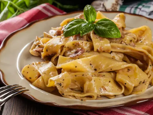 Breite, cremige Pappardelle-Nudeln mit Speck und Kräutern, garniert mit Basilikum.