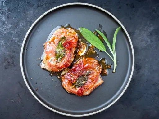Zwei in Prosciutto eingewickelte Fleischstücke mit Salbei, glasiert und auf einem Teller serviert. Ein köstliches Beispiel für italienische Gerichte.