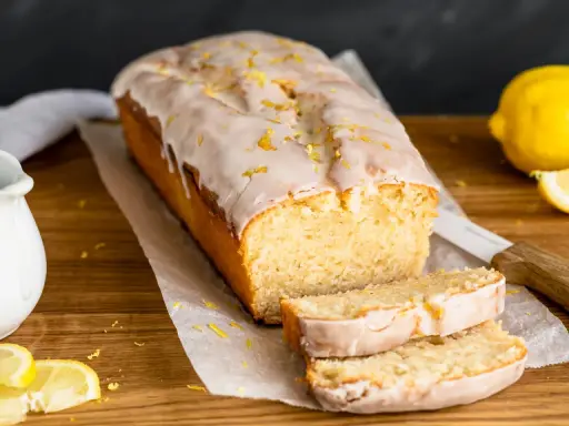 Saftiger veganer Zitronenkuchen mit Zuckerguss und Zitronenschale bestreut. Ein köstlicher Genuss!