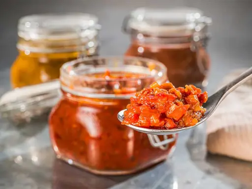 Ein Löffel voll leckerem Tomaten-Chutney, perfekt für Ihr nächstes Tomaten-Chutney-Rezept. Im Hintergrund stehen weitere Gläser mit Chutney.