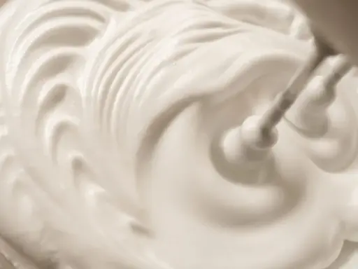 Schlagende Sahne wird mit einem Handmixer zu steifen Spitzen aufgeschlagen, bereit für köstliche Desserts.