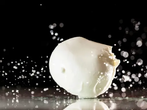 Ein frischer Fior di Latte, der auf einer spiegelnden Oberfläche liegt, umgeben von Wassertropfen und Bokeh-Lichtern.