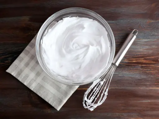 Schneebesen neben Schüssel mit steif geschlagenem Eiweiß. Eine tolle Alternative, wenn man fragt, was kann man statt Sahne nehmen.