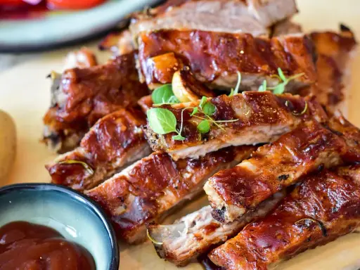 Saftige Spareribs mit glänzender Marinade, garniert mit frischen Kräutern. Dazu eine Schale BBQ-Sauce und eine Kartoffel.