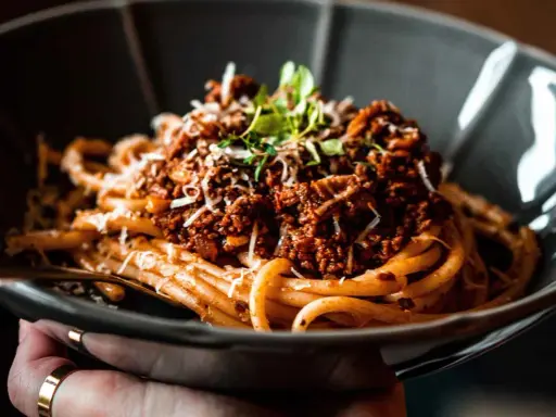 Eine Schüssel mit herzhaftem Pasta al Ragu, garniert mit frischen Kräutern und geriebenem Käse.