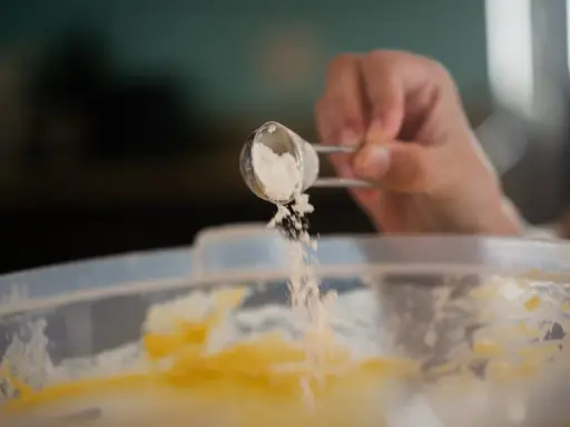 Eine Hand streut Natron aus einem Löffel in eine Schüssel mit Teig. Perfekt für das Backen!