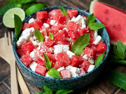 Erfrischender Wassermelonensalat mit Feta und Minze, perfekt für ein leichtes sommersalat rezept. Dazu passen Limettenspalten und Holzbesteck.