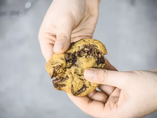 Hände halten einen weichen Chocolate Chip Cookie, der gerade zerbrochen wurde. Das Innere ist voller geschmolzener Schokolade. Ein perfektes Cookies Rezept weich.