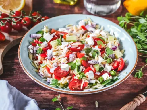 Frischer Kritharaki Salat mit Tomaten, Gurken, Feta und roten Zwiebeln, garniert mit Kräutern. Ein leichter Genuss!