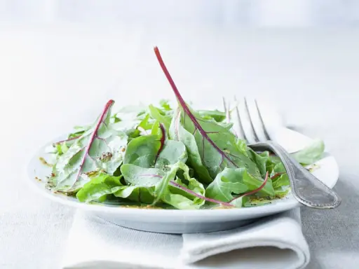 Frischer mangold salat mit roten Stielen, beträufelt mit Dressing, auf einem Teller mit einer Gabel.
