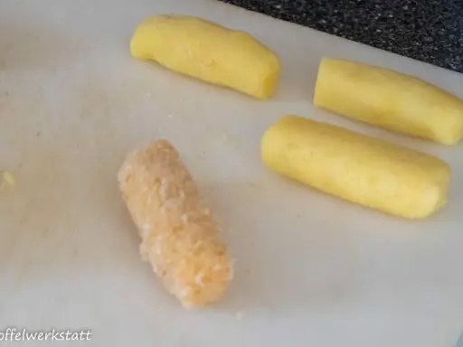 Vier Kartoffelstäbchen liegen auf einem Schneidebrett. Eines ist bereits paniert, die anderen drei warten darauf, dass sie **kroketten selber machen** können.