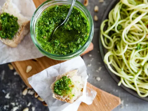 Frisches Basilikumpesto rezept in einem Glas, daneben Brot mit Pesto und eine Portion Spaghetti. Perfekt für ein schnelles Mittagessen.